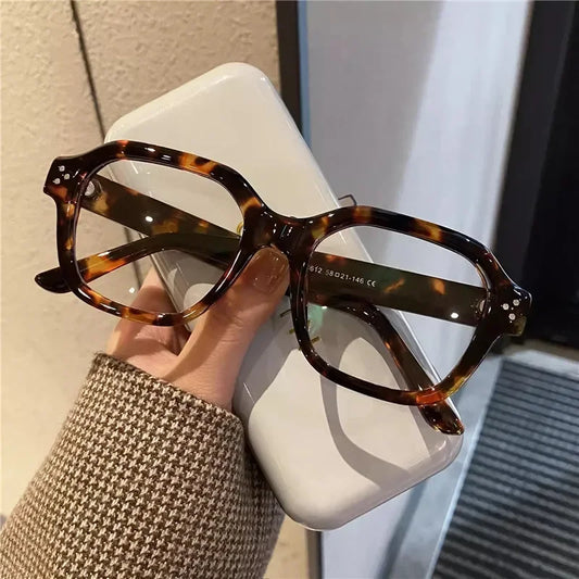 Élégance Lunettes Femme stylish tortoiseshell glasses held with a phone case on a textured surface.